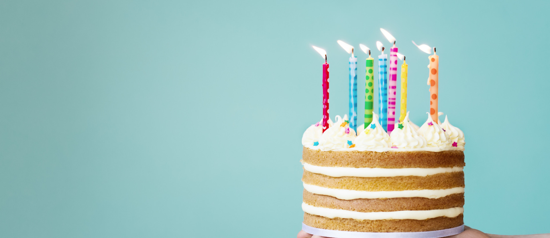 bolo de aniversário com velas coloridas encima em um plano de fundo azul